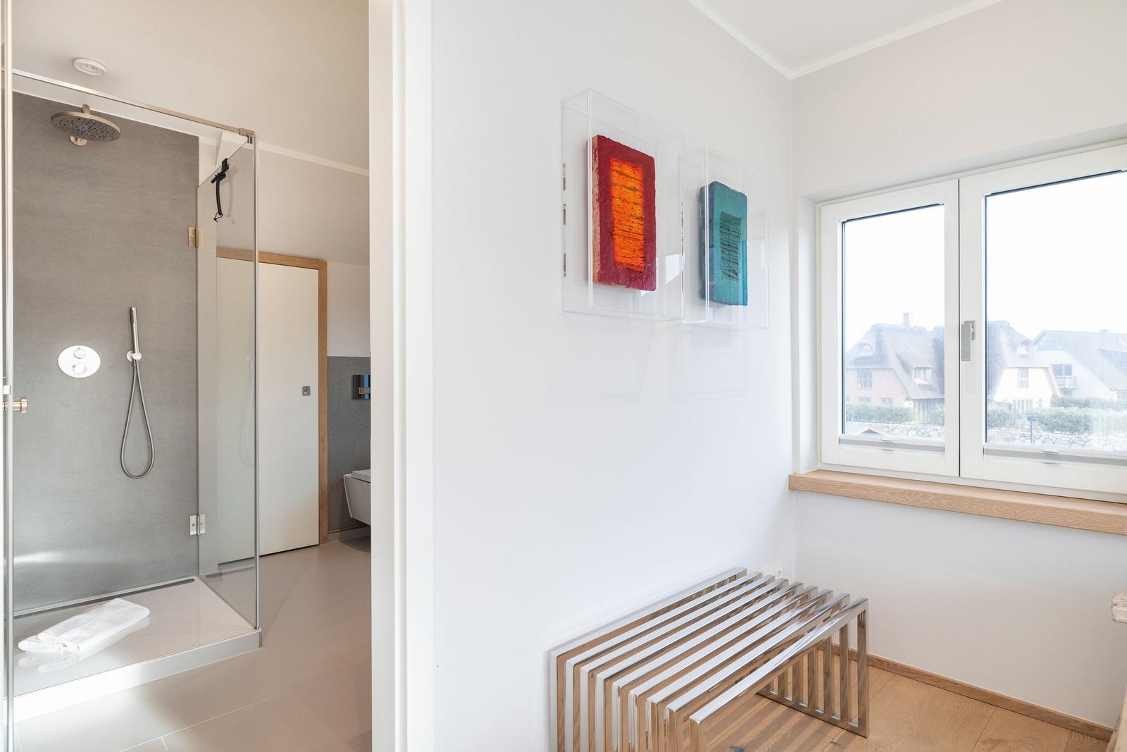 Shower area with glass wall and window with view of rooftops.