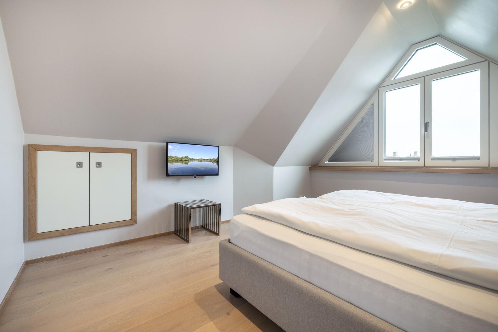 Bedroom with sloped ceiling, bed, TV, and window.