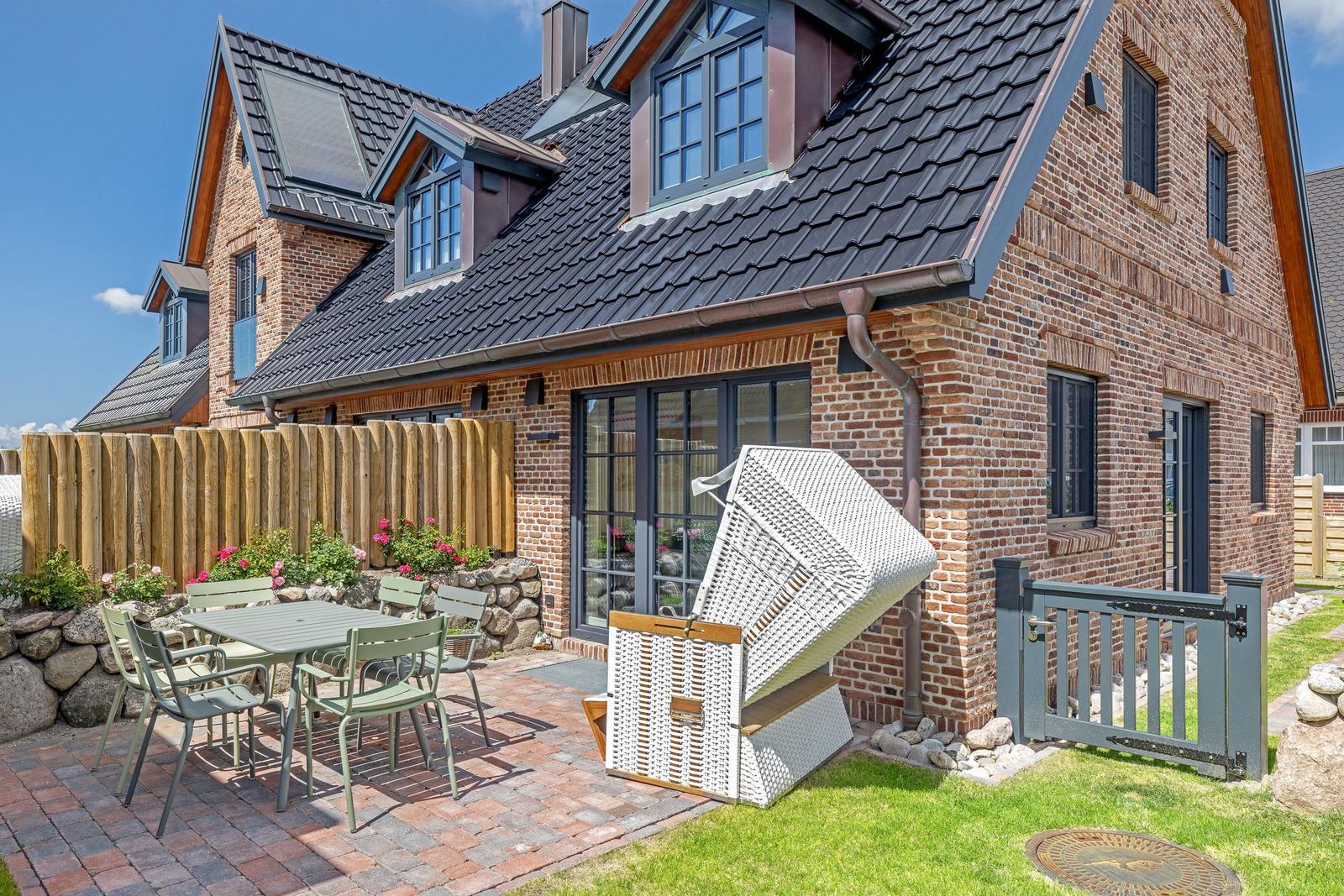 Haus mit Garten, Terrasse und Liegestuhl. Holzzaun und Steinmauer umgeben den Außenbereich.