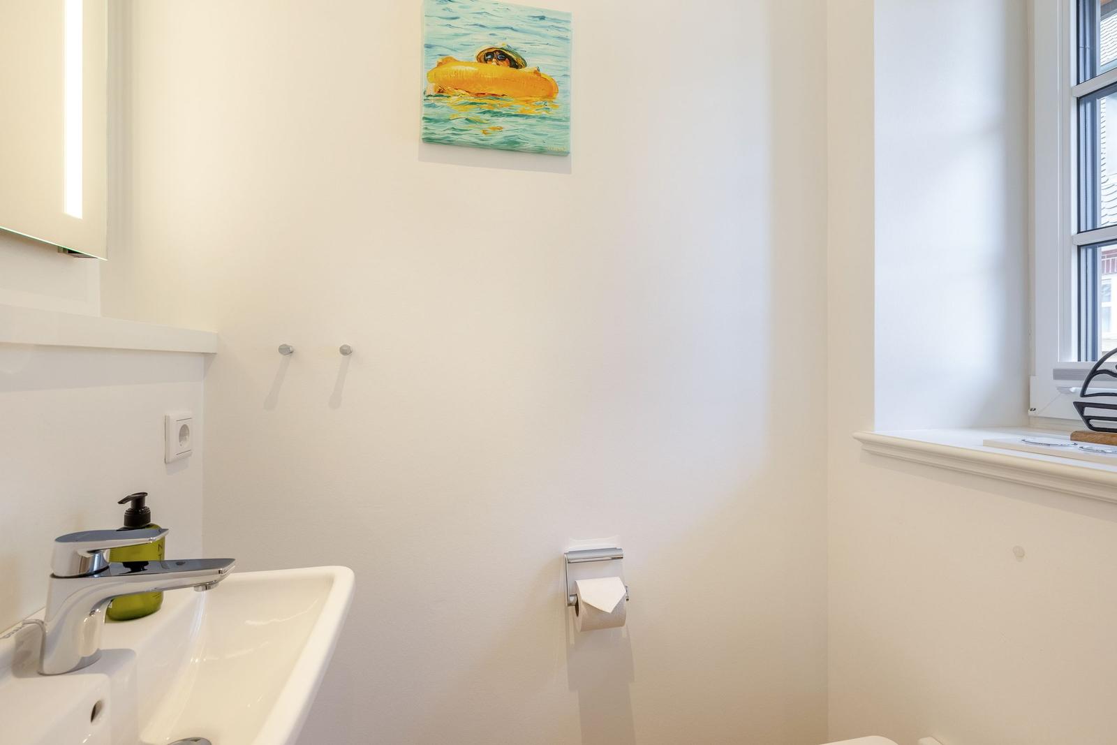 Badezimmer mit Waschbecken, Toilettenpapierhalter und Wandbild.