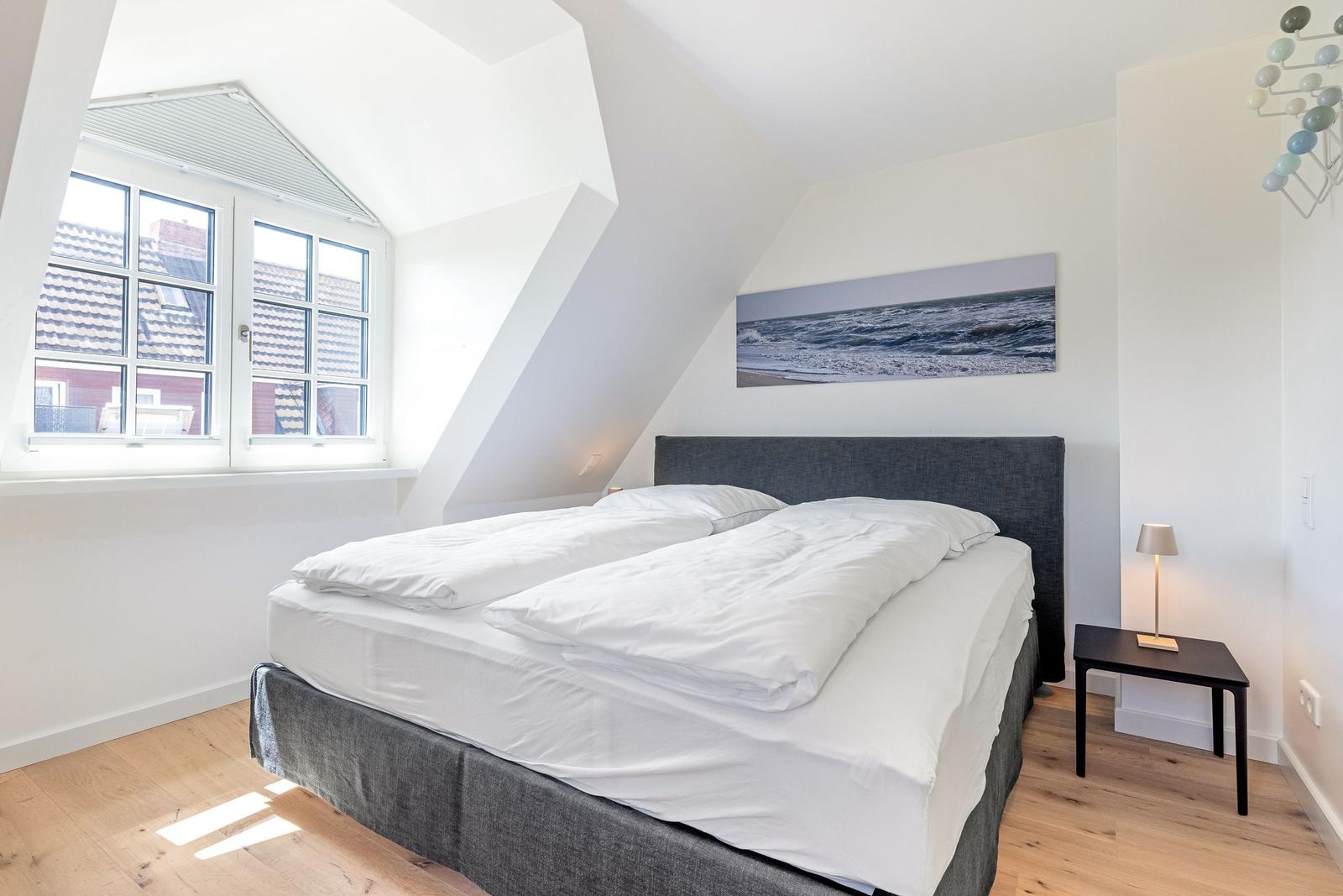 Schlafzimmer mit Doppelbett, Fenster und Wandbild.