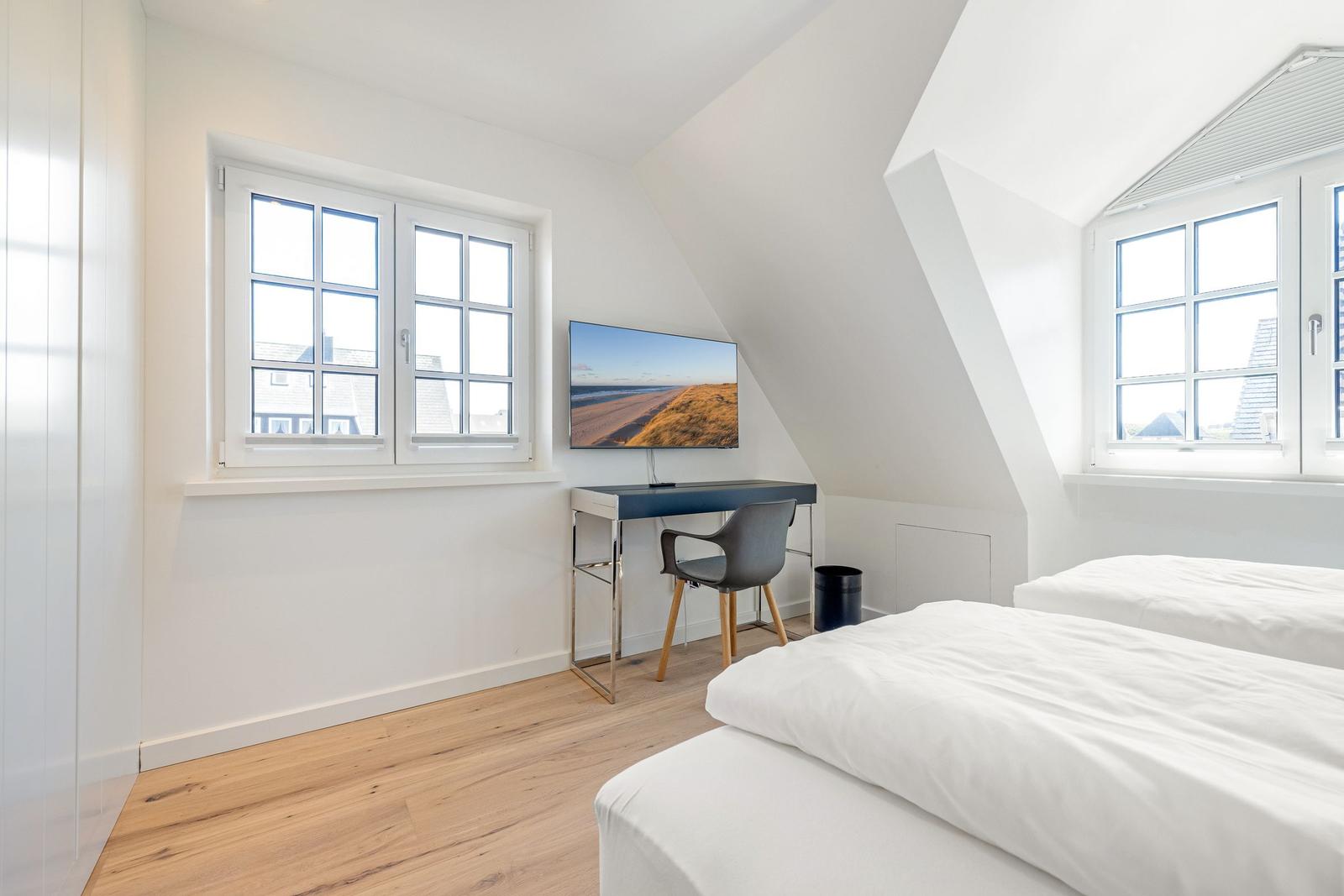 Zimmer mit zwei Betten, Schreibtisch und TV unter Dachschrägen mit Fenstern.