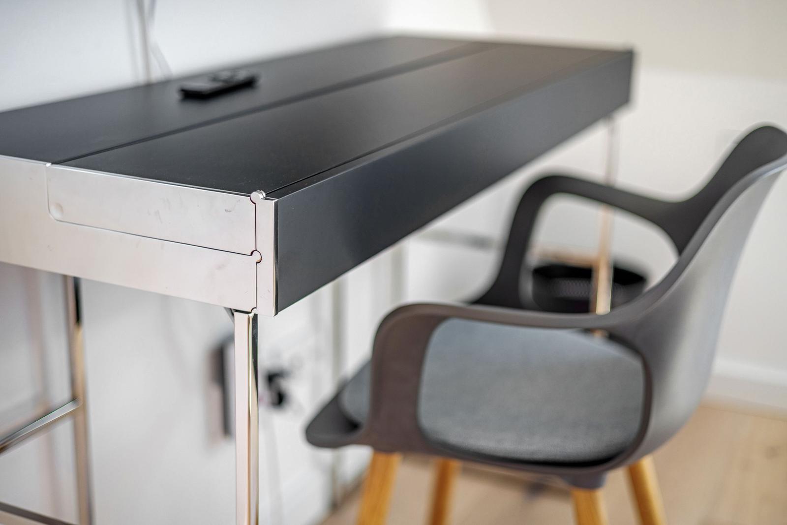 Schwarzer Schreibtisch mit Metallbeinen und Stuhl mit grauer Sitzfläche.