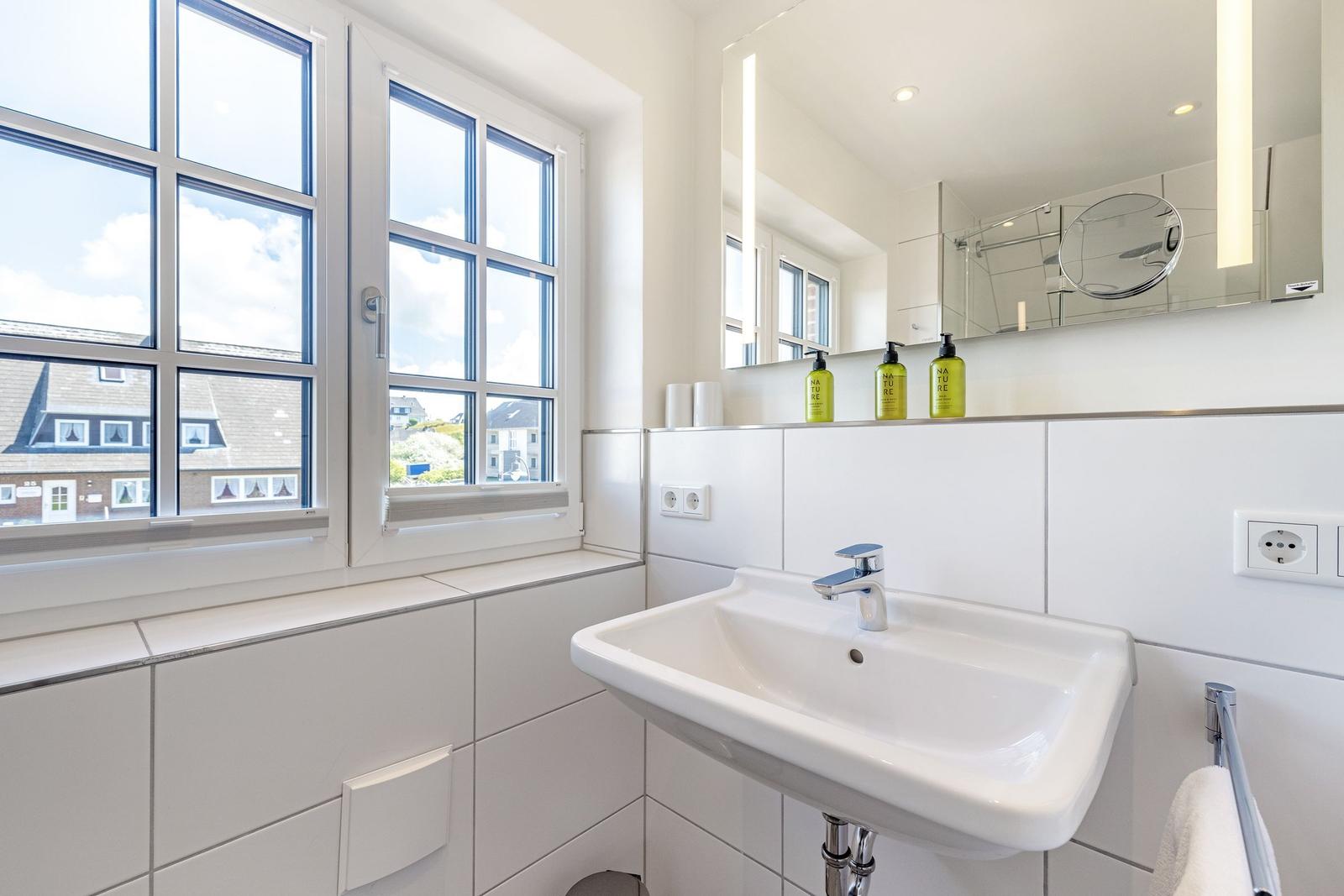 Badezimmer mit Waschbecken, Spiegel und Fenster zur Aussicht.