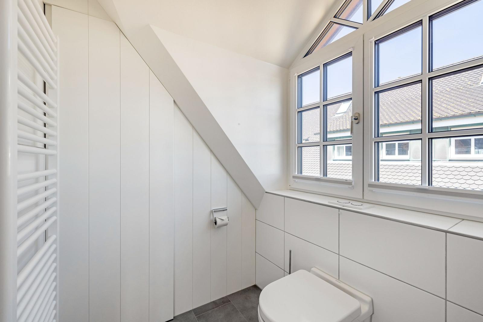 Badezimmer mit Toilette, Fenster und Heizkörper an der Wand.