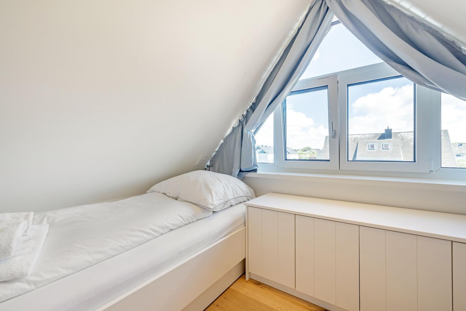 Ein Schlafzimmer mit Einzelbett, Fenster und Schrank.