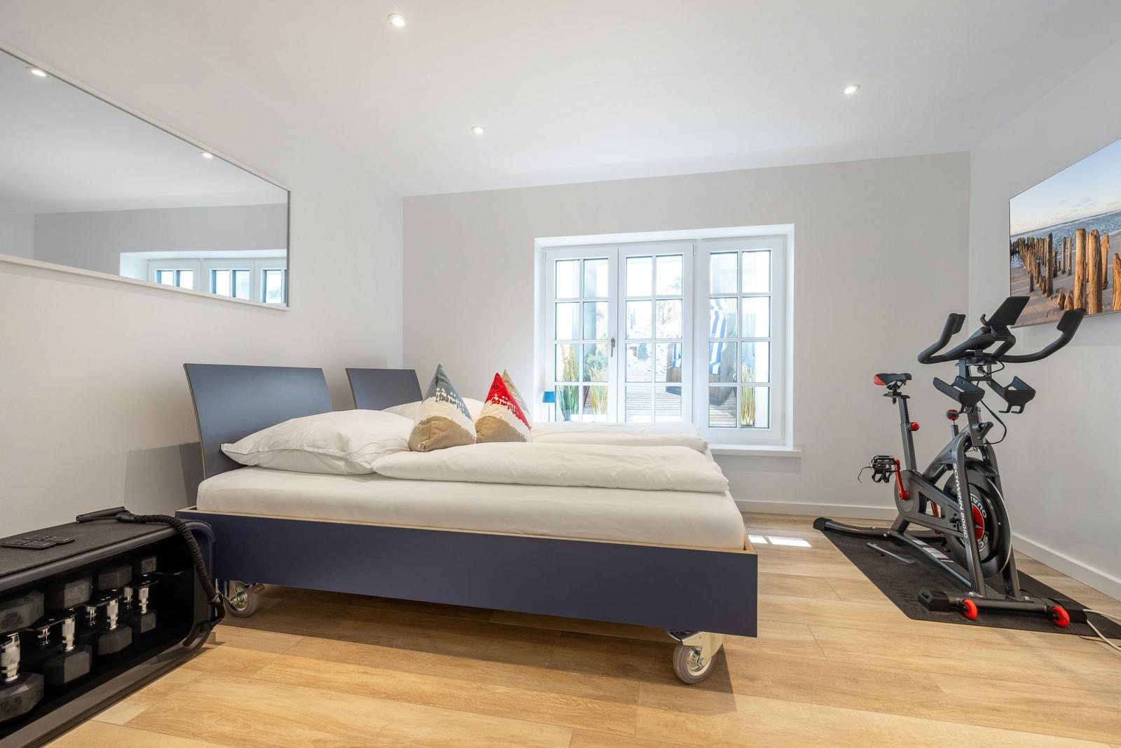 Schlafzimmer mit Bett, Spiegel, Fitnessrad und Fenster
