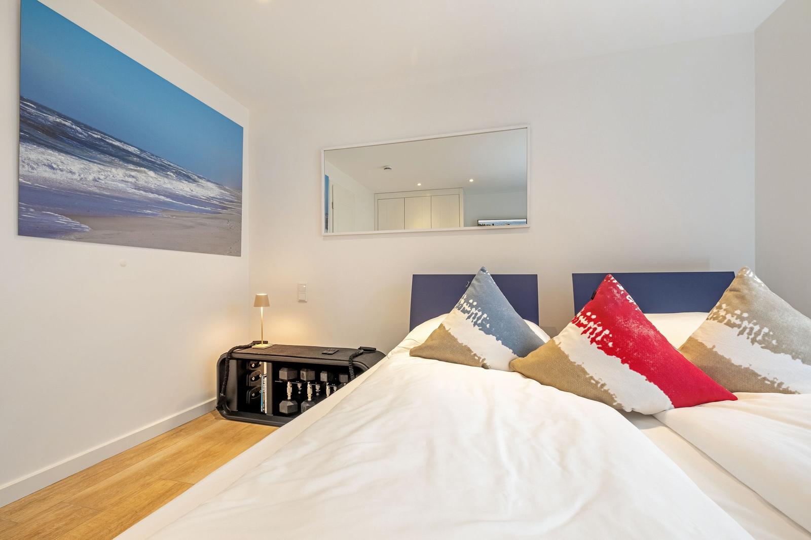 Schlafzimmer mit Bett, Kissen, Wandbild und Spiegel.