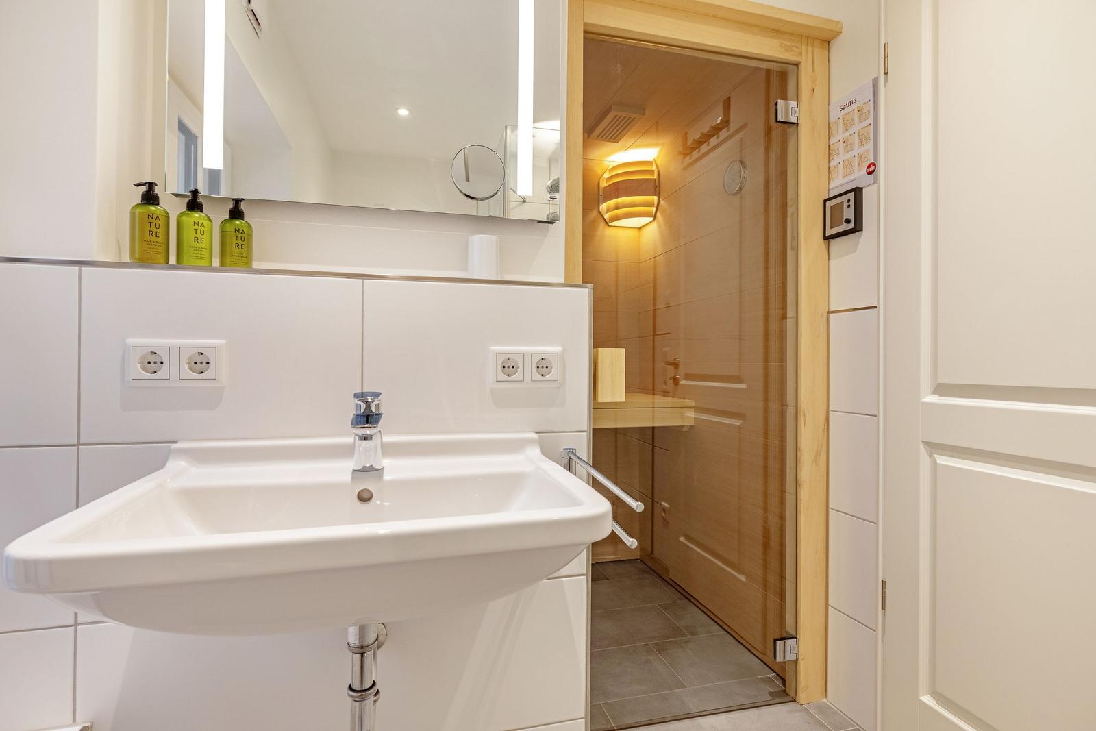 Waschbecken mit Spiegel und Sauna im Hintergrund.