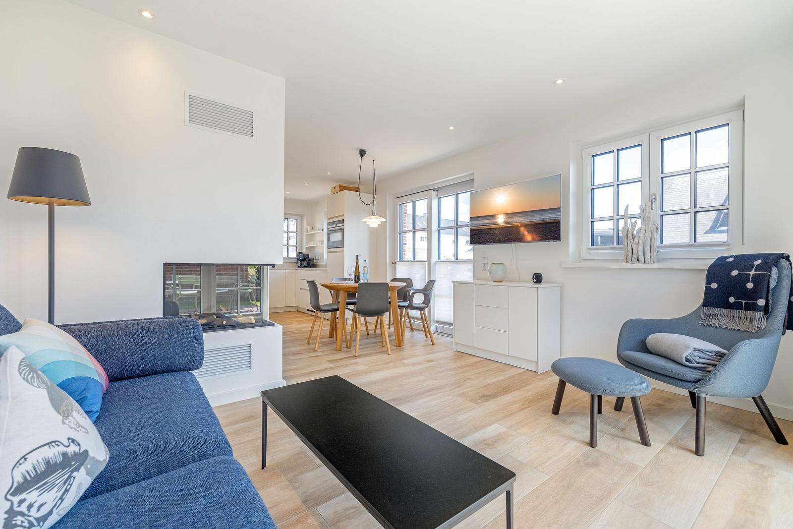 Wohnzimmer mit Sofa, Sessel und Esstisch. Kamin und Fenster sichtbar.