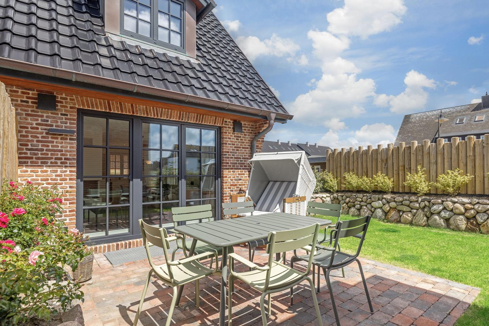 Terrasse mit Tisch, Stühlen und Liegestuhl. Hinterhof mit Steinmauer und Holzzaun.