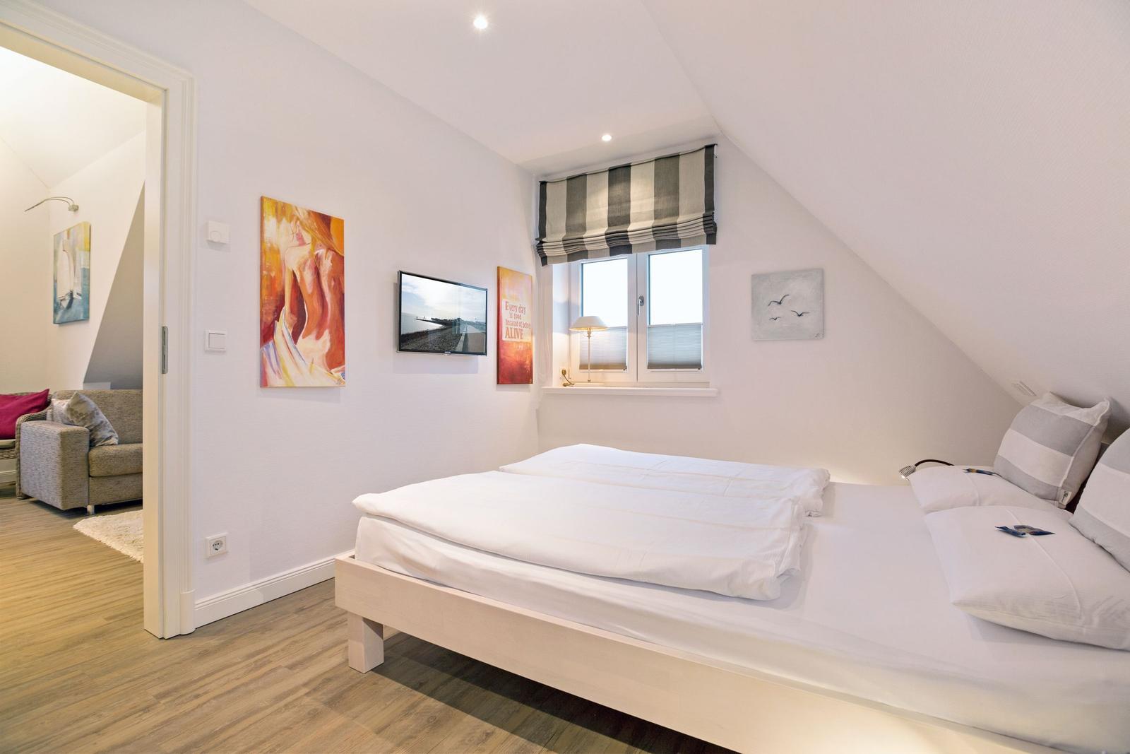 Schlafzimmer mit Doppelbett, Fenster und Kunstwerken an der Wand.