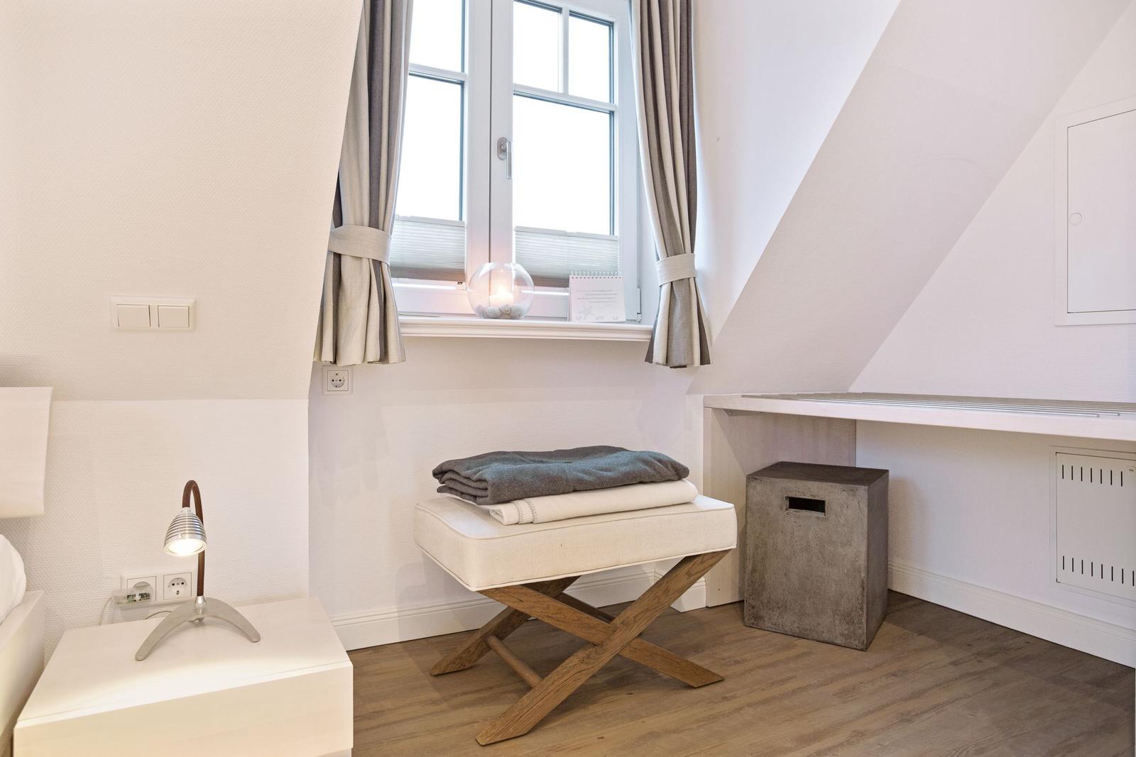 Schlafzimmer mit Fenster, Nachttisch, Stuhl und Schreibtisch.