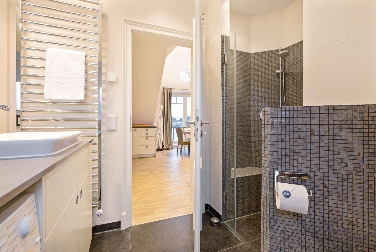 Badezimmer mit Dusche, Waschbecken und Blick in Wohnbereich.
