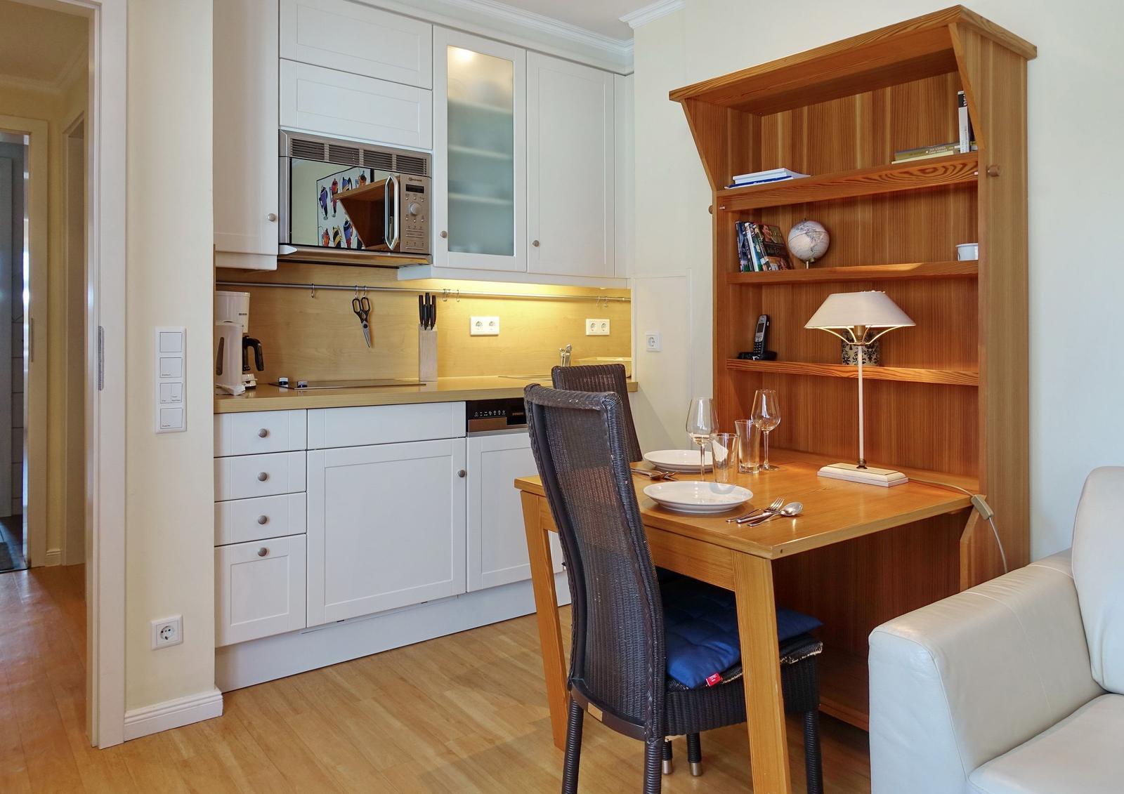 Kitchen with dining area and bookshelf. Wooden table, chairs, and white cabinets.