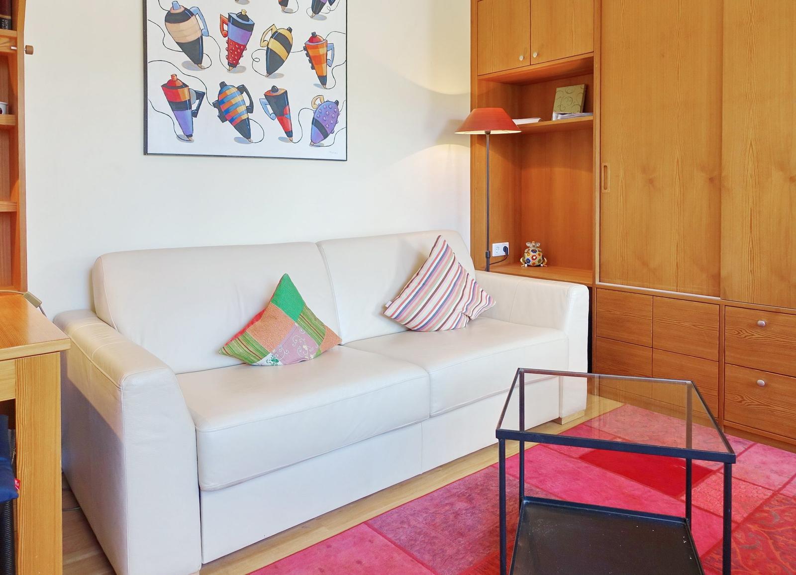 White sofa with cushions on red rug in front of wooden furniture.