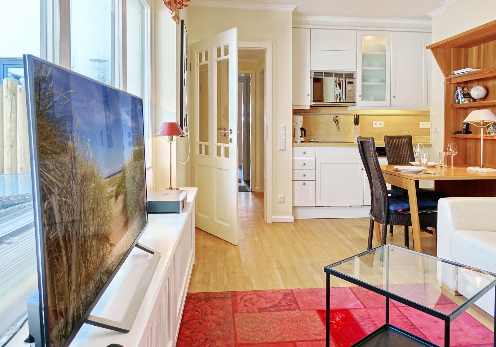 Apartment with kitchen, dining area, and TV. Wooden floor and red rug.