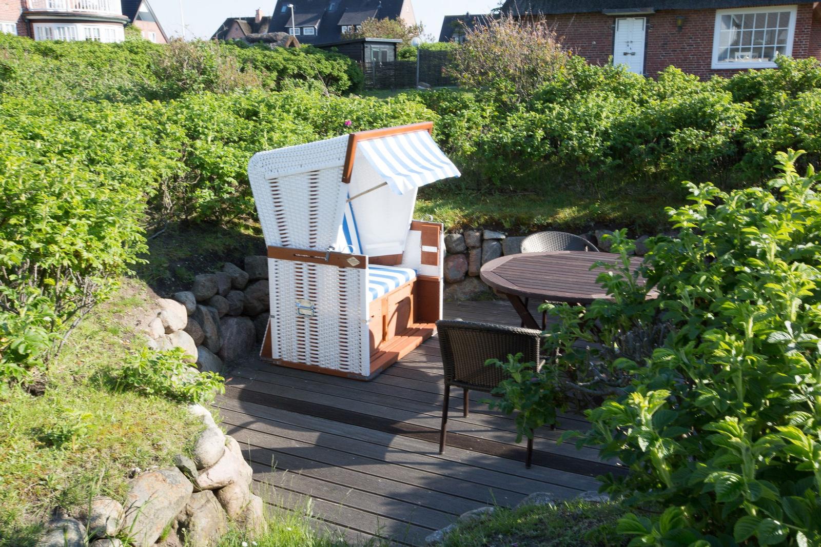 Deck with beach chair, table and chairs surrounded by greenery.