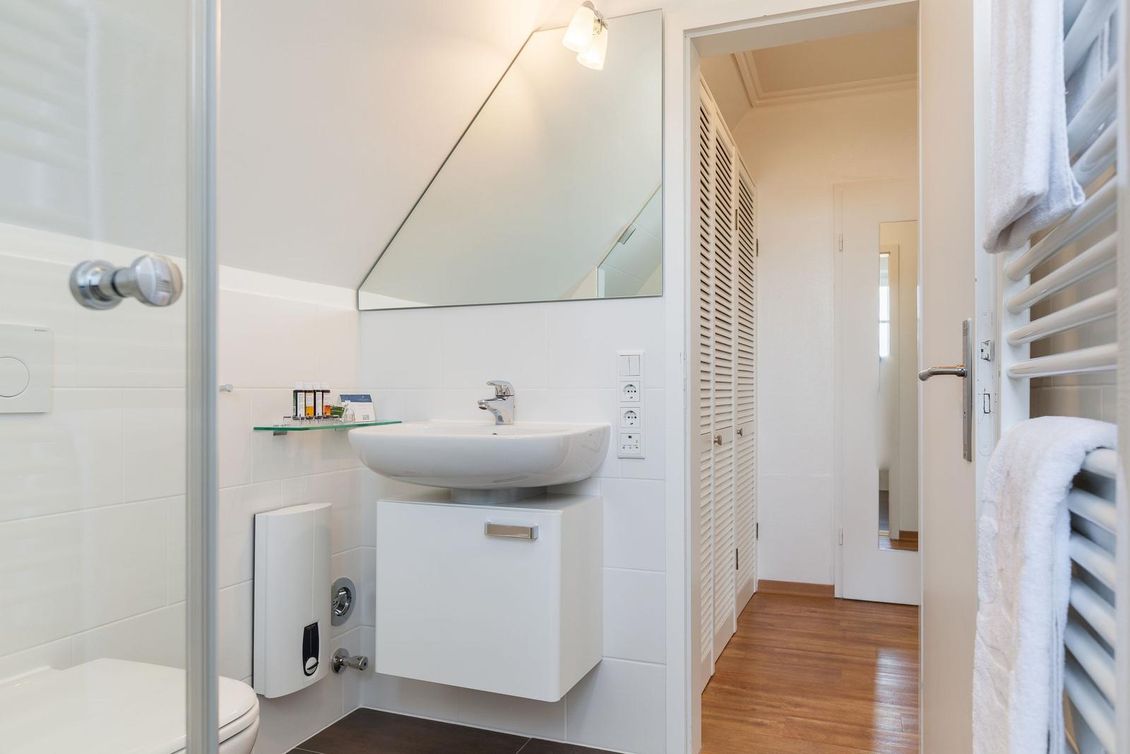 Bathroom with shower, sink, and mirror. Wooden floor and towel warmer.