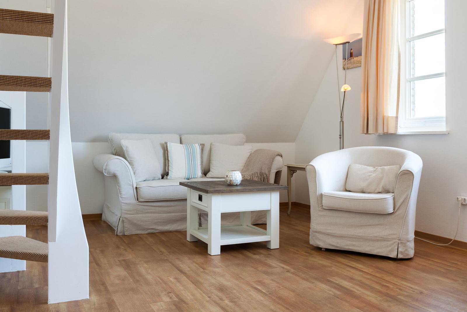 Living room with sofa, armchair, and table. Wooden floor and window with curtains.