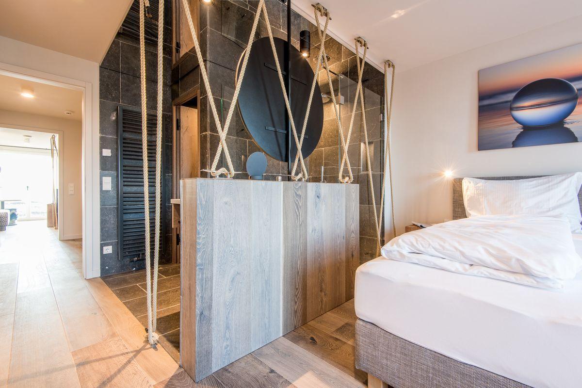 Schlafzimmer mit Bett, Holzboden und moderner Dusche mit Seilgestell.