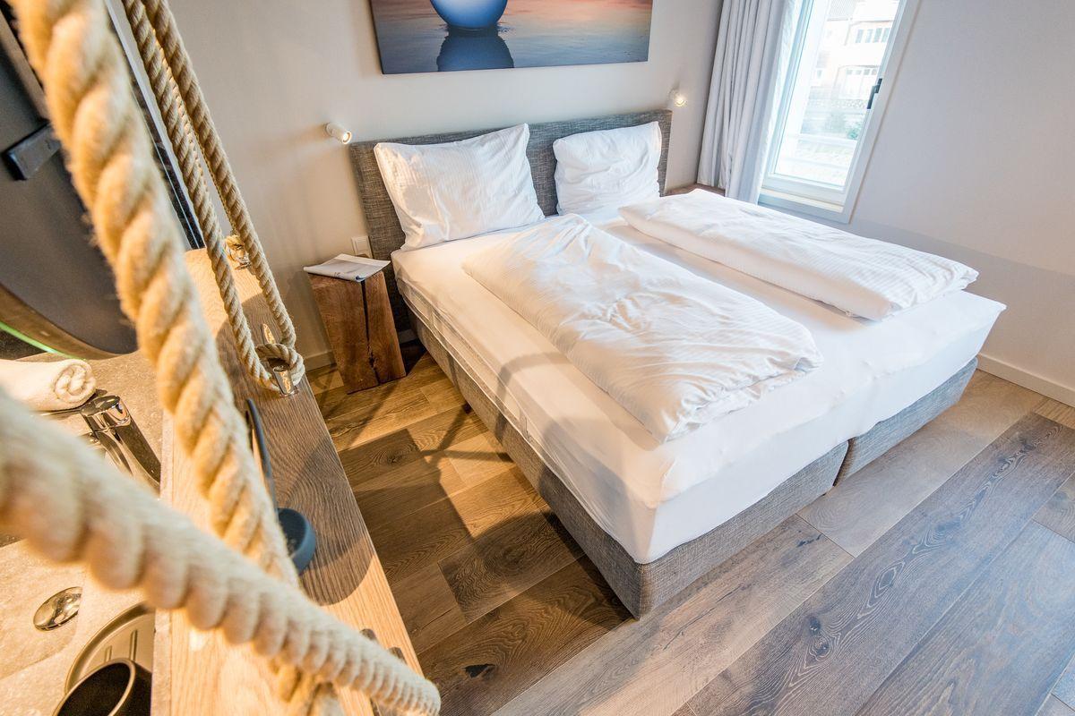 Schlafzimmer mit Doppelbett, Holzboden und Fenster. Seil als Dekoration sichtbar.