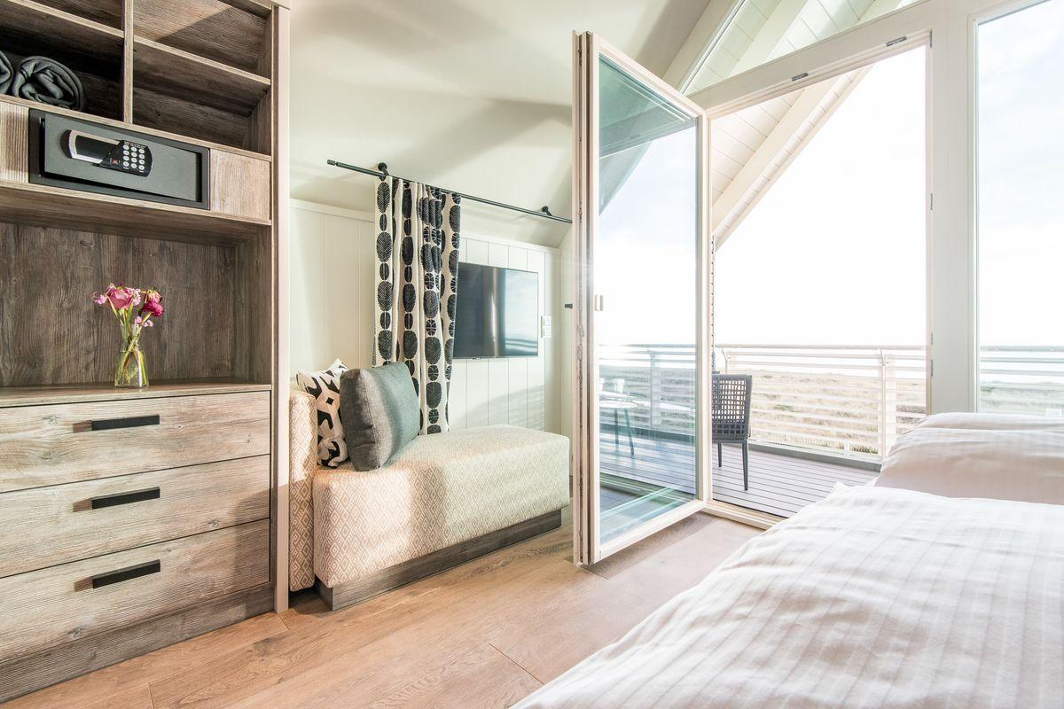 Schlafzimmer mit Balkon, Schrank und TV. Holzboden und große Fenster.