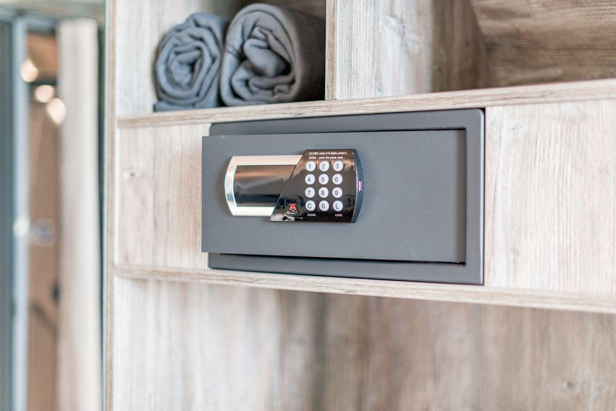 Ein digitaler Safe ist in einem Holzregal eingebaut, darüber liegen zwei gefaltete Handtücher.