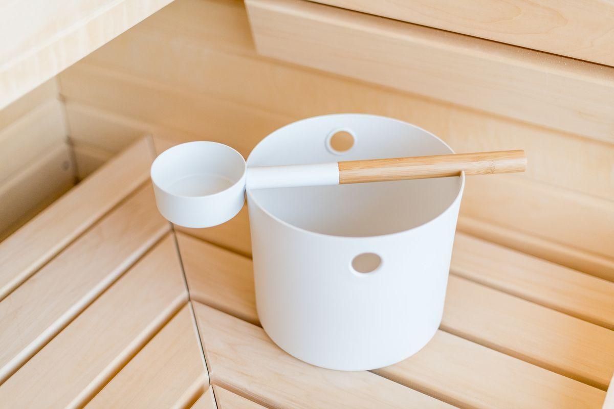Weißer Eimer mit Holzlöffel auf Holzbank in Sauna