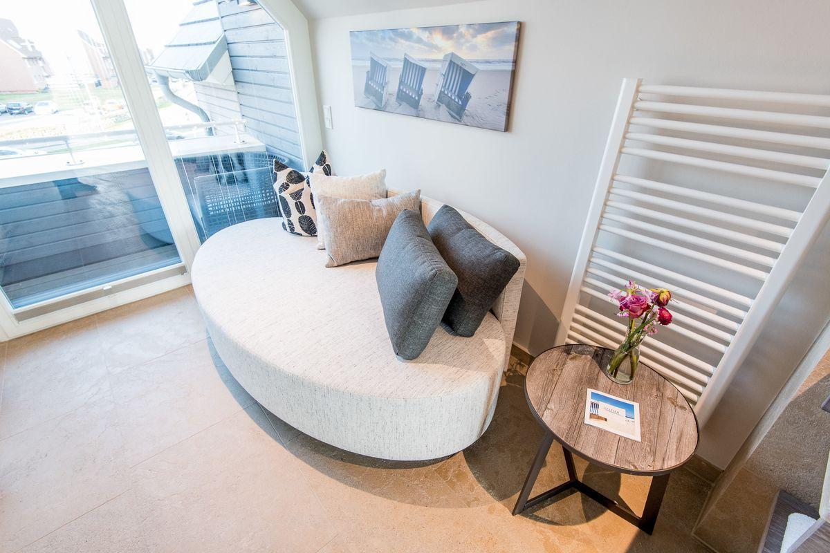 Rundes Sofa mit Kissen, kleiner Tisch und Wandheizung neben Glasfront.