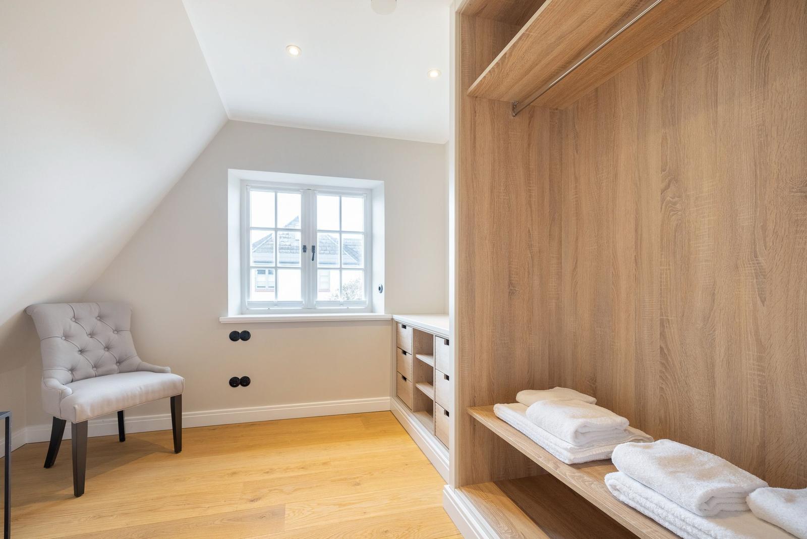 Schlafzimmer mit Holzboden, Kleiderschrank und Sitzgelegenheit.