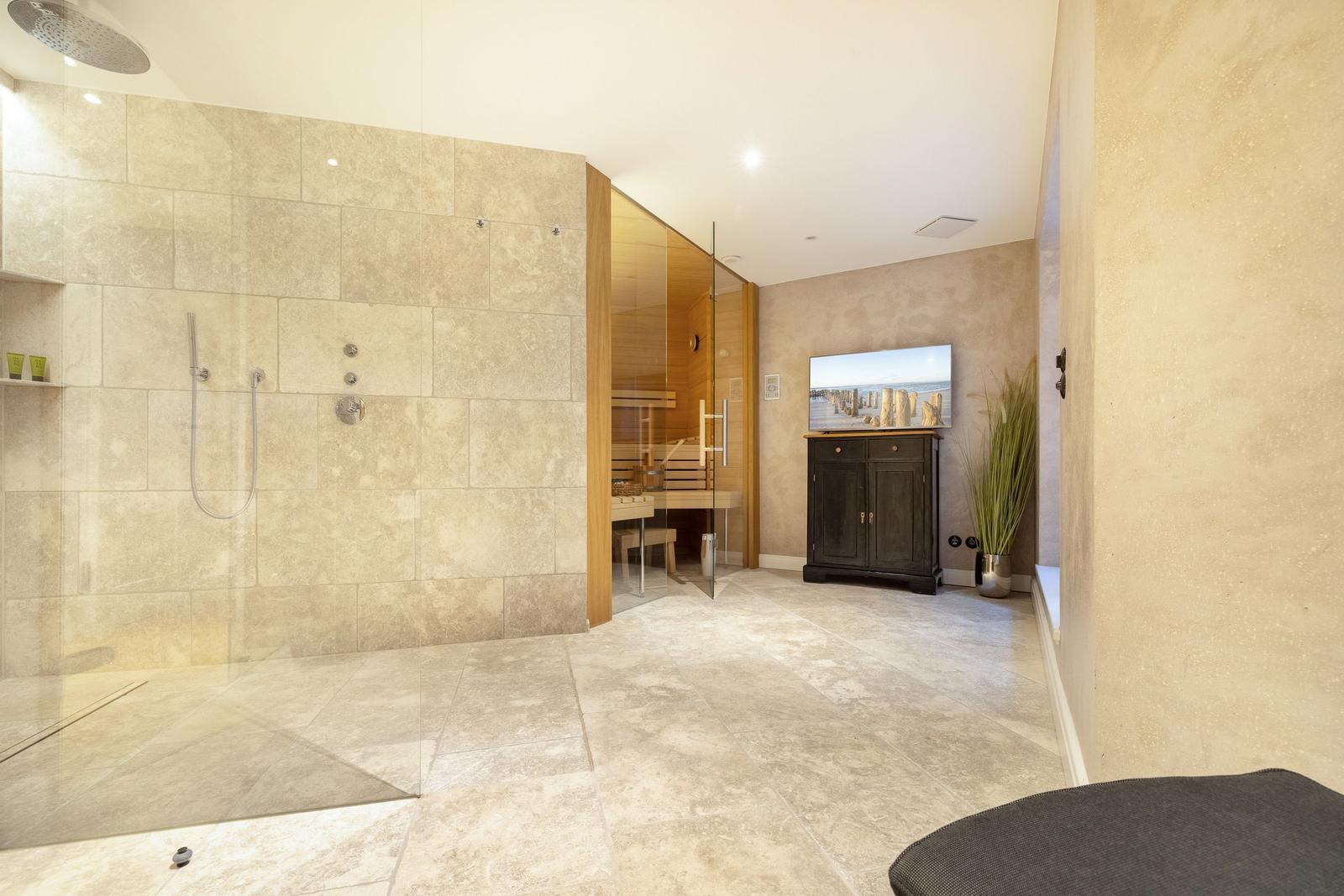 Dusche mit Regenduschkopf, Sauna und Fernseher im Raum.