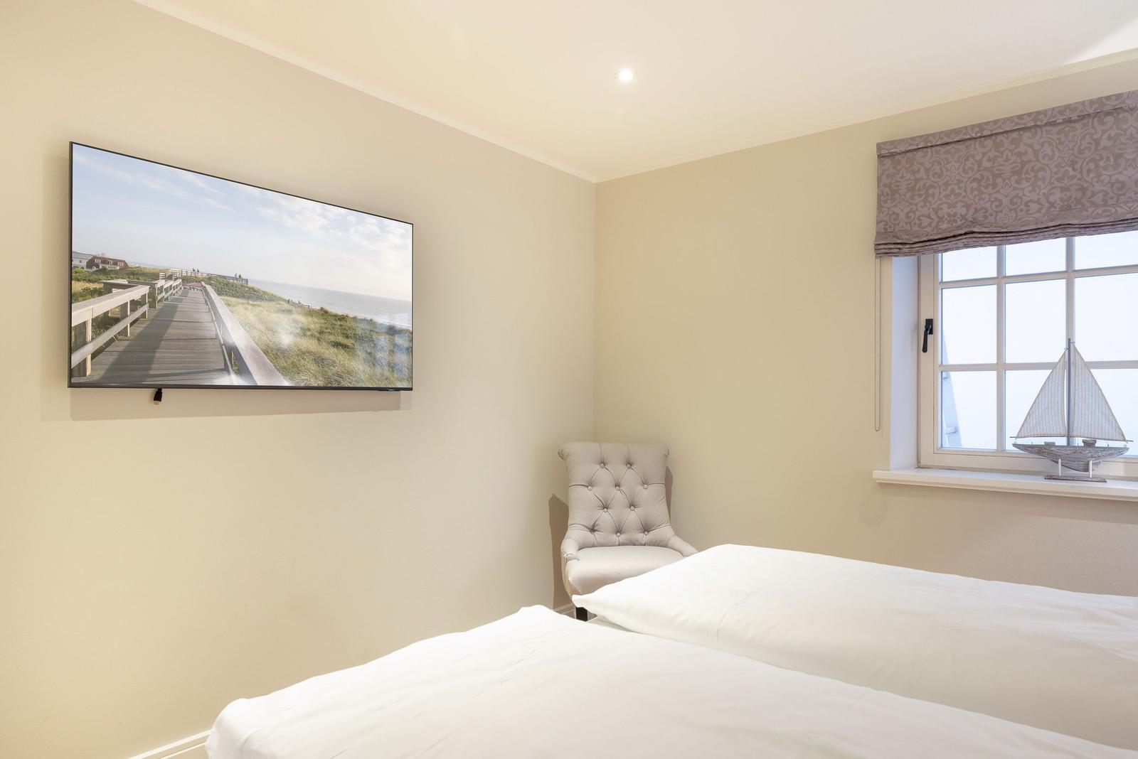 Schlafzimmer mit Bett, Sessel und Fenster mit Segelschiffmodell.