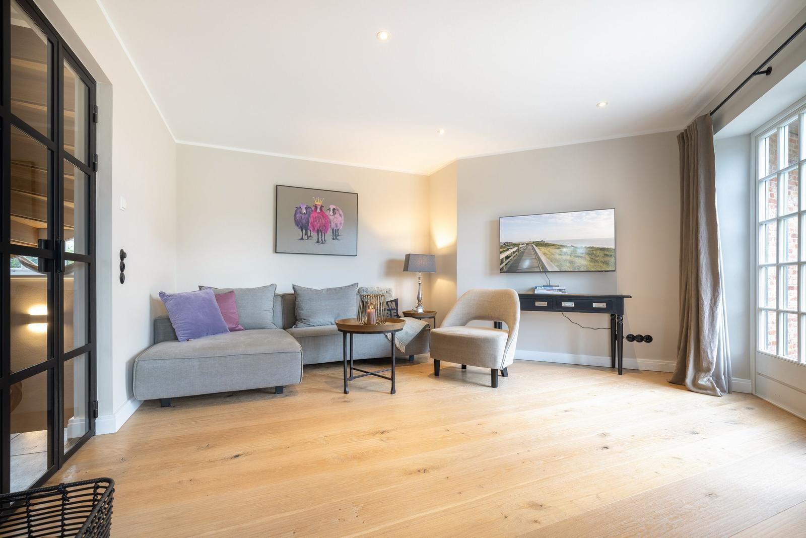Wohnzimmer mit Sofa, Sessel, Fernseher und Holzboden.