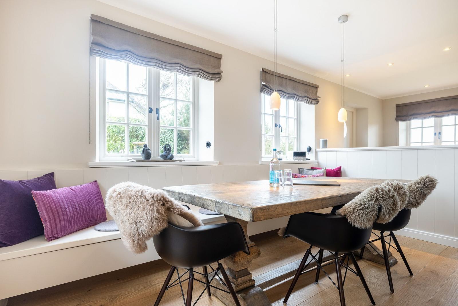 Esszimmer mit Holztisch, schwarzen Stühlen und Fensterbank mit Kissen.