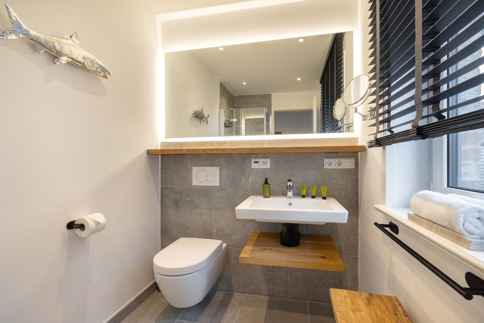 Bad mit Waschbecken, Toilette und Spiegel über Holzregal.