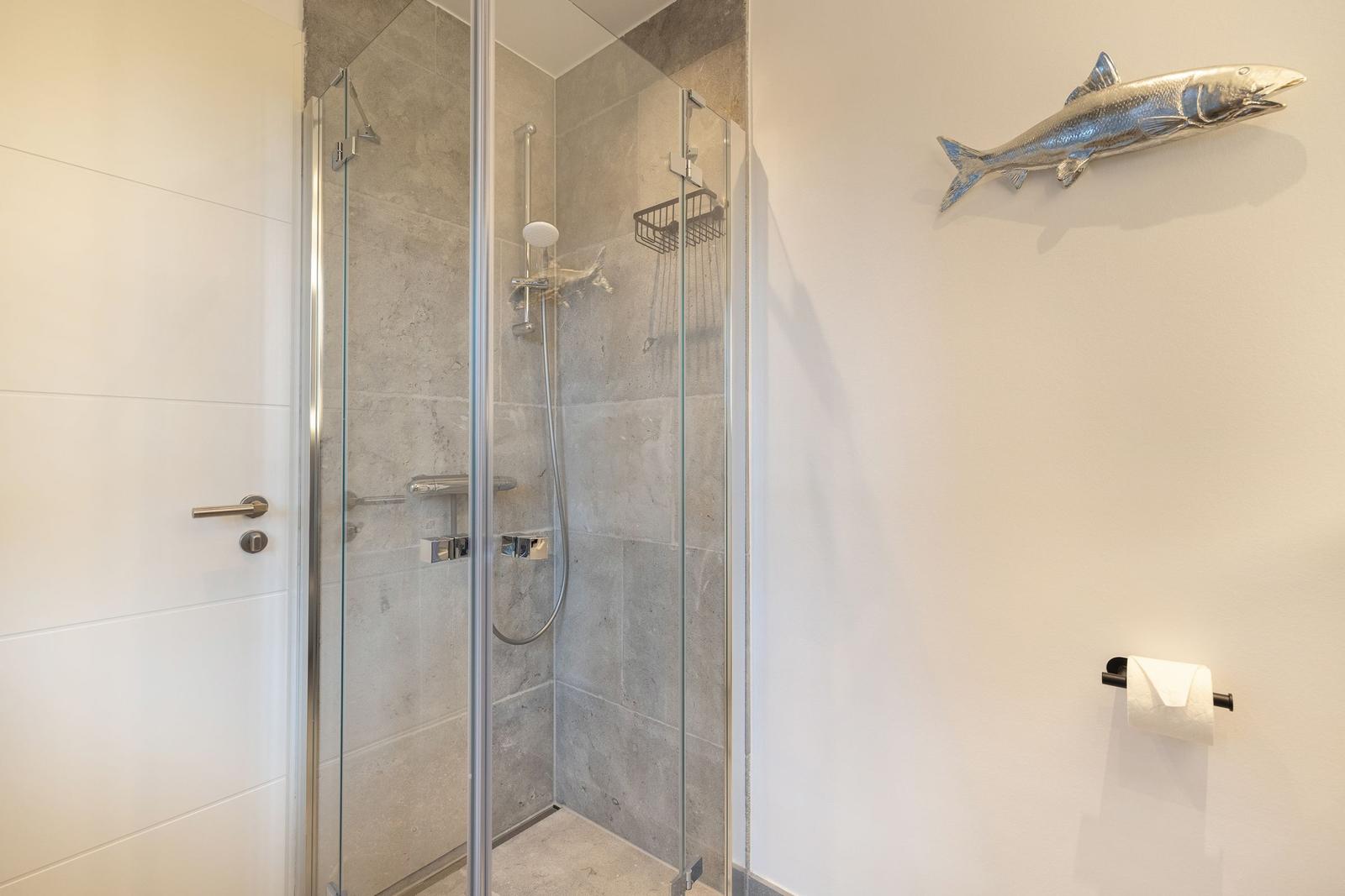 Dusche mit Glaswand, Wandhalterung und Fischdekoration.