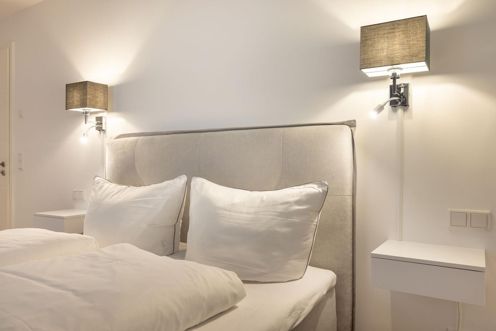 Schlafzimmer mit Bett, Kopfteil und Wandlampen.