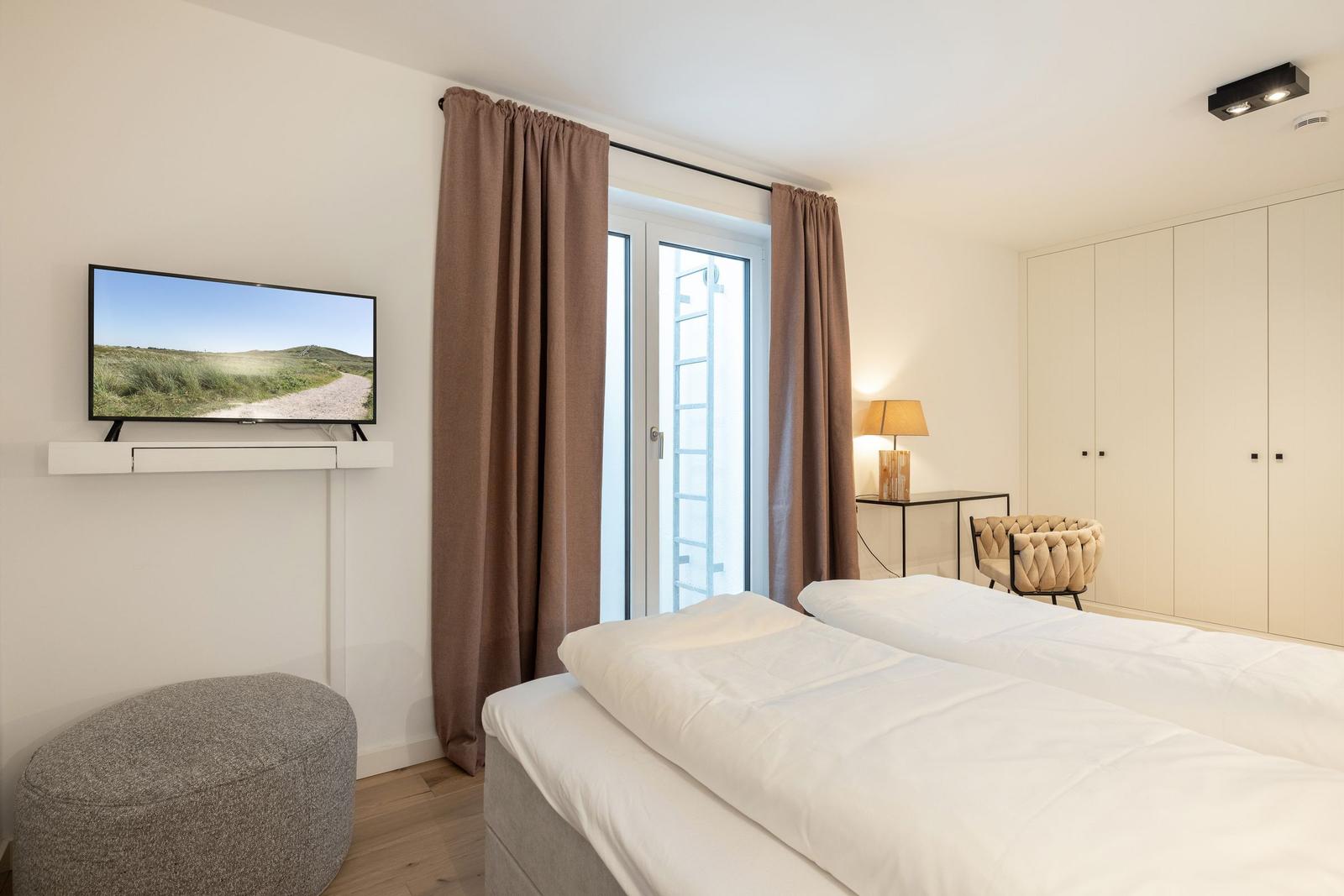 Schlafzimmer mit Doppelbett, Fernseher und Fenster mit Vorhängen.