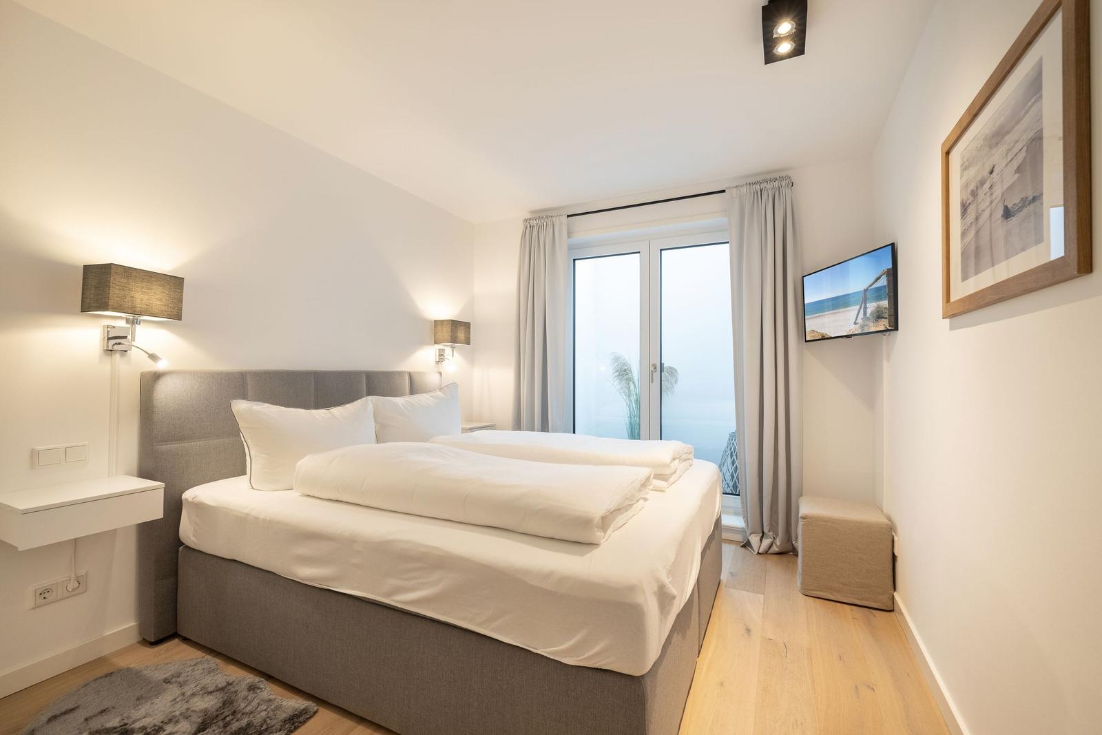 Schlafzimmer mit Bett, Fenster und Fernseher.