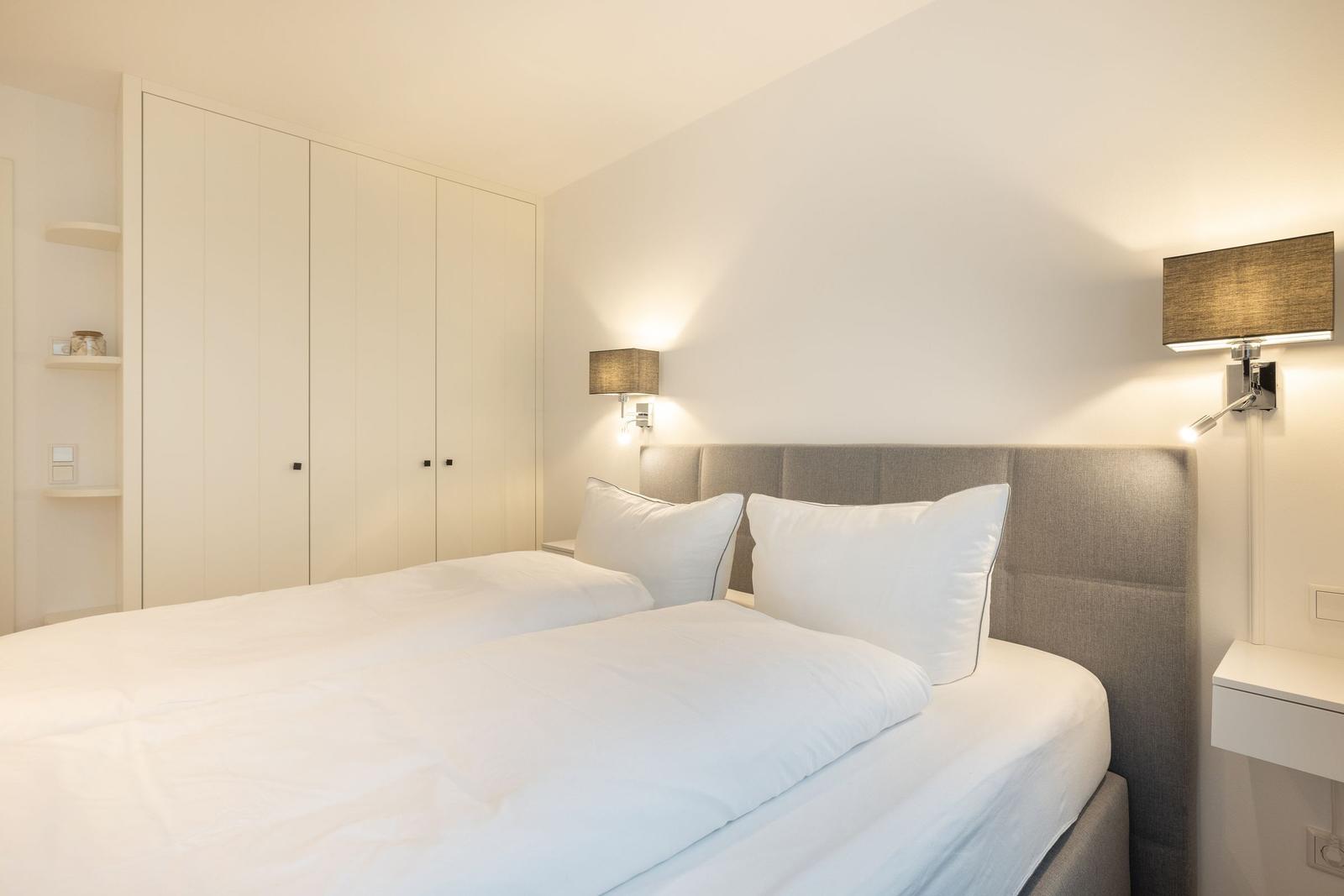 Schlafzimmer mit Bett, Kleiderschrank und Wandlampen.