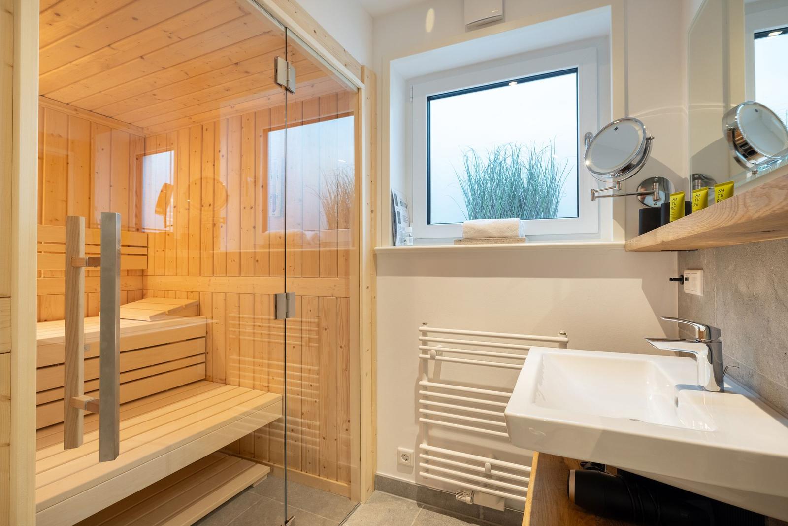 Dusche mit Sauna, Waschbecken und Fenster mit Pflanze.
