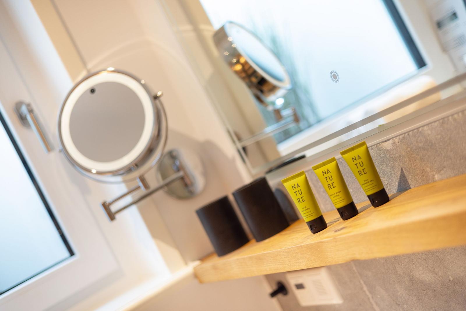 Badezimmer mit beleuchtetem Spiegel und gelben Pflegeprodukten auf Holzoberfläche.