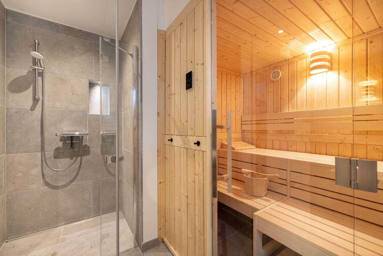 Dusche mit Glaswand und Sauna mit Holzbank und Eimer