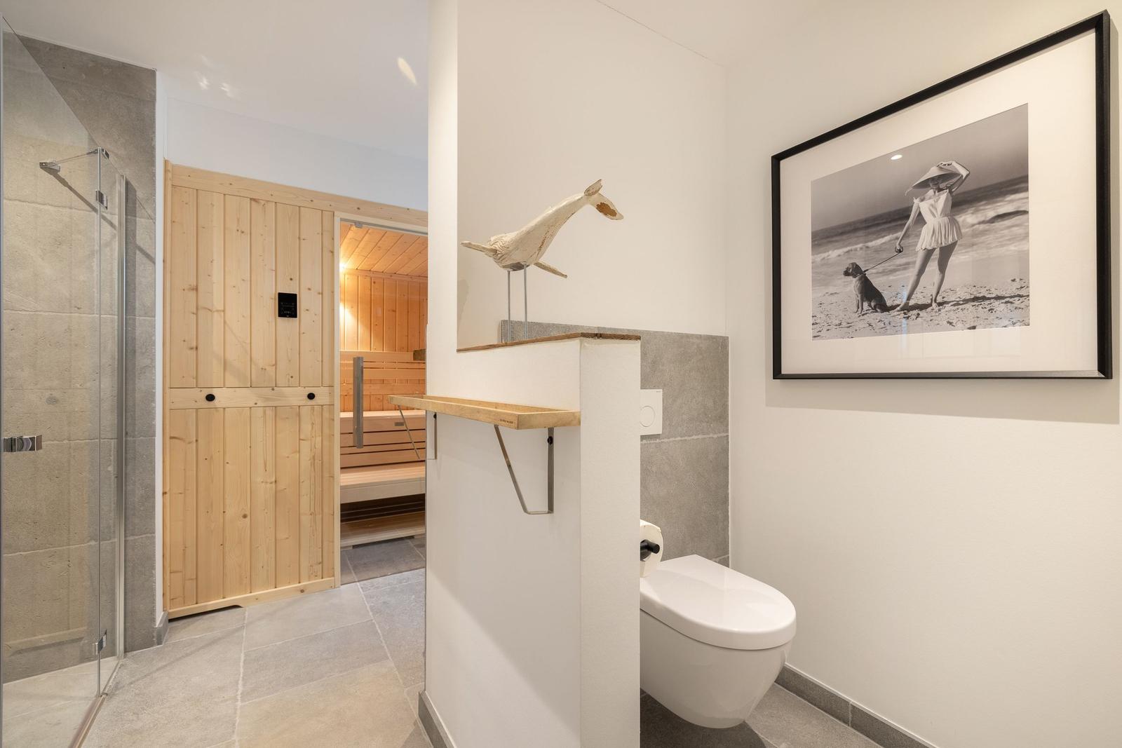 Bad mit Dusche, Toilette und Sauna im Hintergrund.