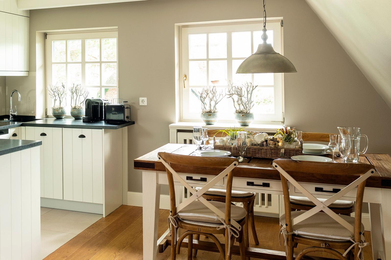 Dining area with wooden table, chairs, and windows. Kitchen with countertop and appliances.