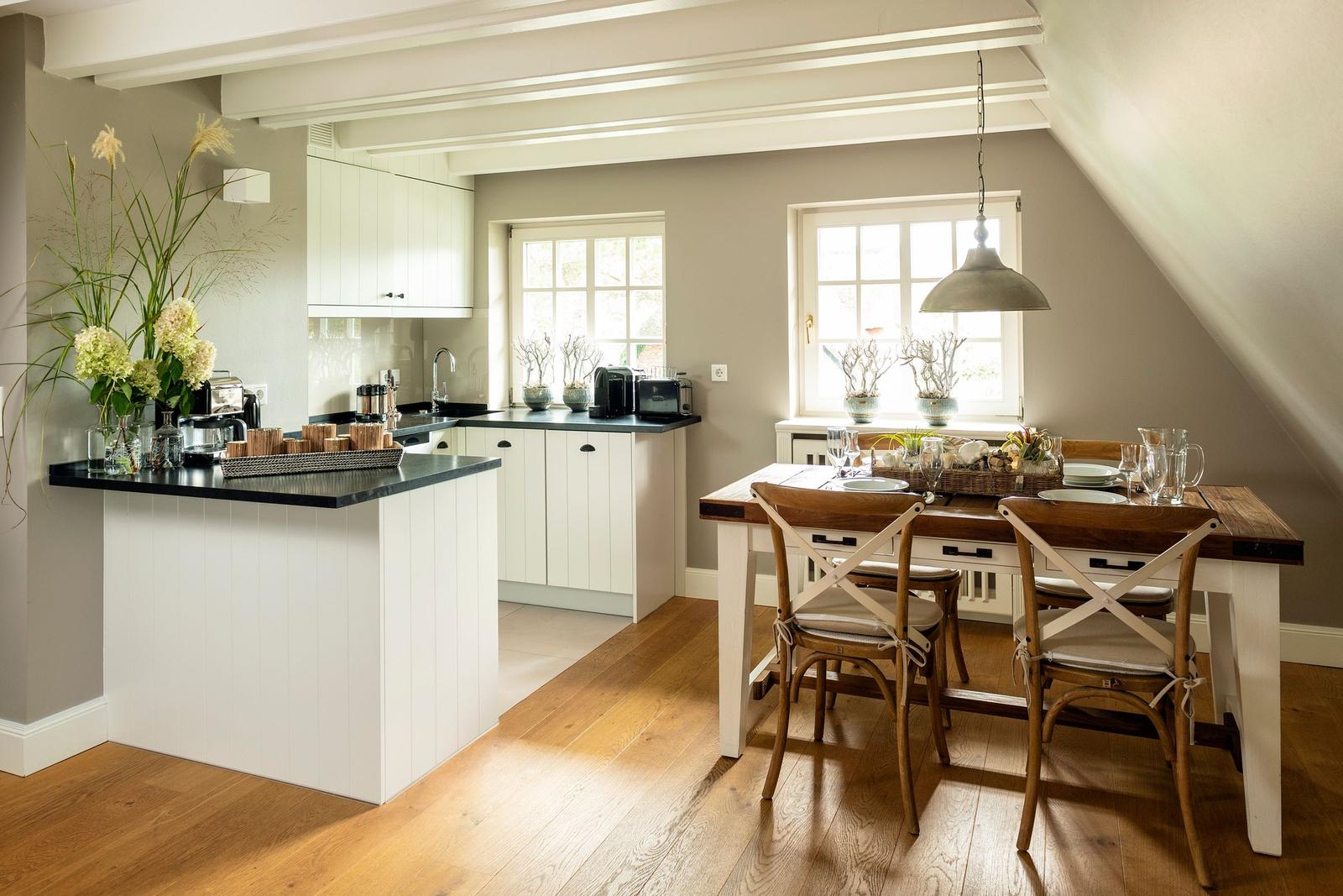 Kitchen with dining area, wooden floor, and white cabinets under sloped ceiling.