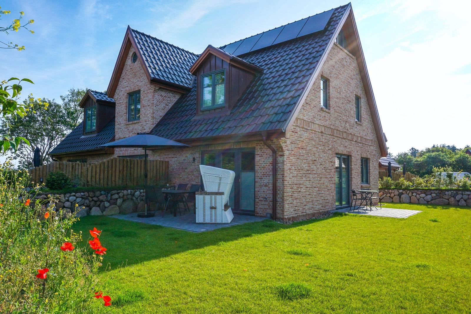Haus mit Steinmauer, Terrasse und Garten. Weiße Gartenmöbel und Sonnenschirm.
