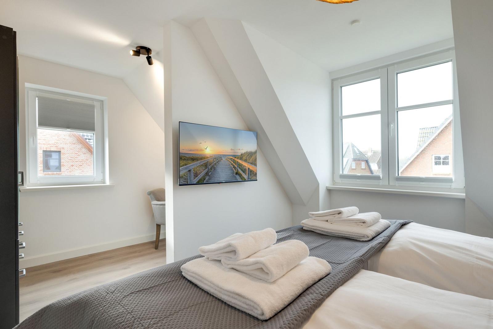 Schlafzimmer mit Dachschrägen, Fenstern und Bett mit Handtüchern.