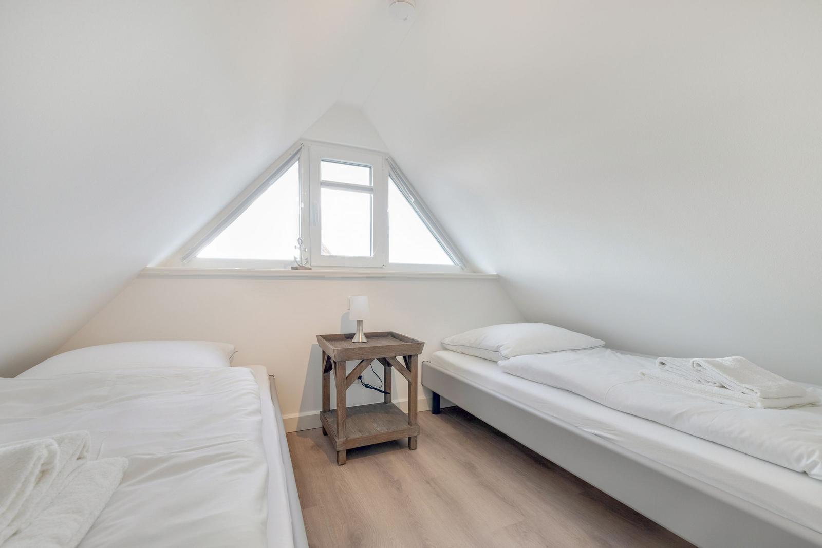 Zwei Betten unter Dachschrägen mit Fenster und Nachttisch.
